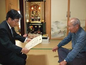 茂野千代子さんご不在のため、ご家族(右)に祝状を手渡す田代町長
