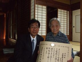 多賀井キクヱさん(右)に祝状を手渡す田代町長