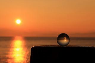 透明なビー玉に夕方の海を映しこんだ写真。