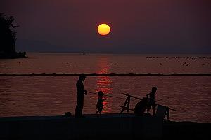 海で夕日を背景に親子が魚釣りをしている写真