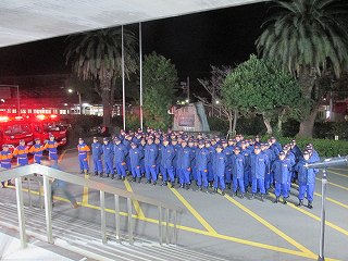 青い防護服を着たたくさんの消防団員が並んでいる写真