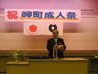 岬町成人祭の幕の下でスピーチをする男性の写真