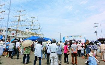 停泊する船とイベントステージを眺める来場者の写真